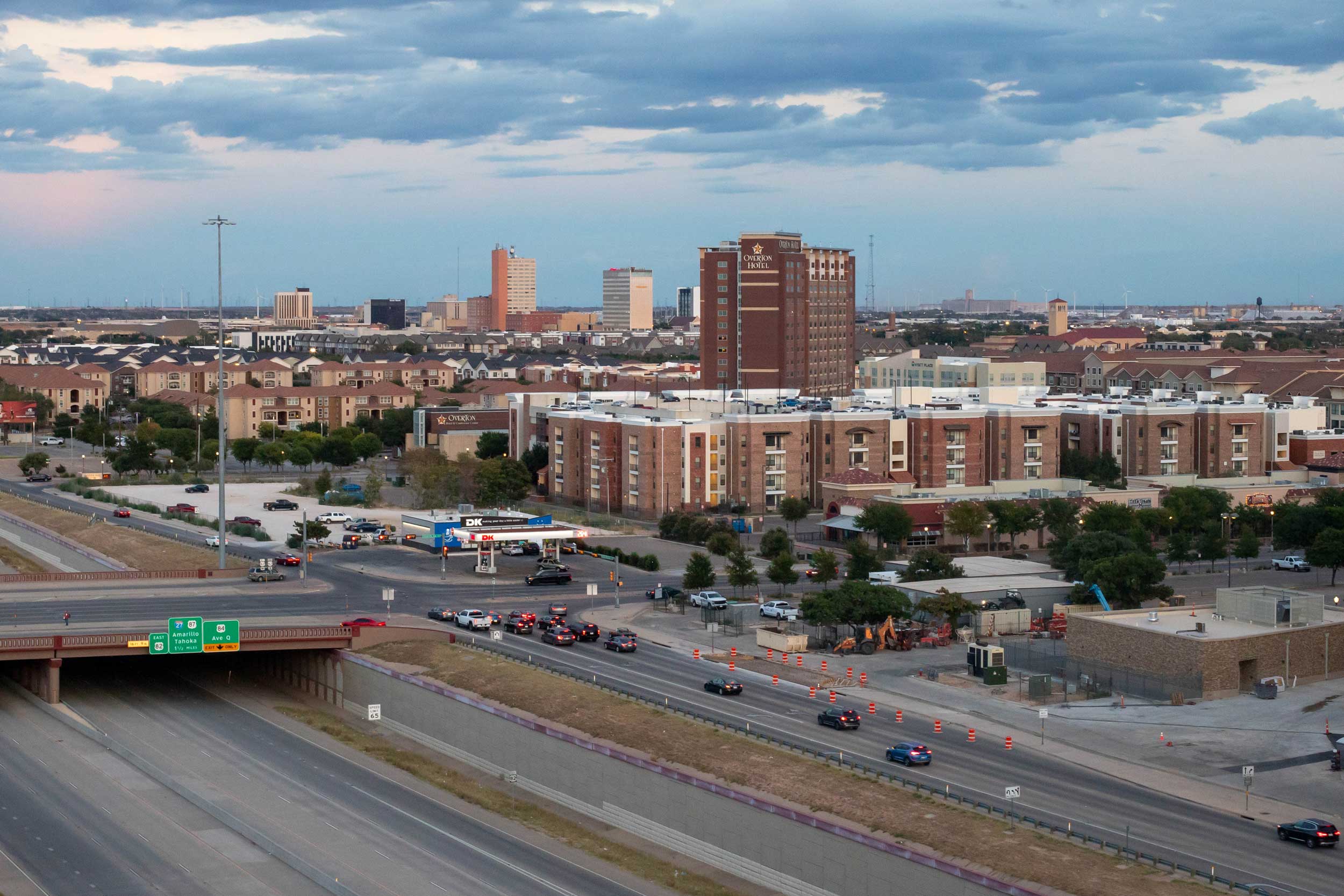 Lubbock, Texas skyline featuring mid-rise buildings, a prominent hotel, and surrounding residential areas during twilight with a highway and traffic in the foreground.