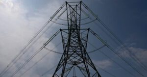 High-voltage power lines and transmission tower against a cloudy sky, symbolizing rising electricity costs in Lubbock, Texas.