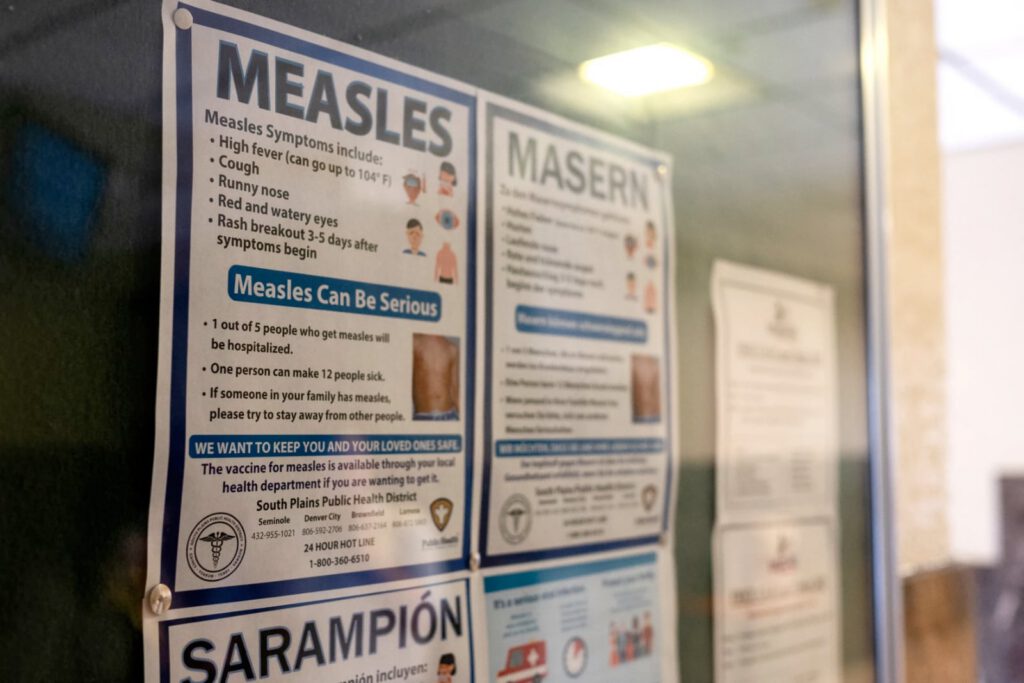 Measles informational poster in English and Spanish at a Texas health facility warning about symptoms, risks, and the importance of vaccination.