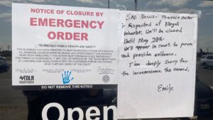 Emergency closure notice from the Texas Department of Licensing and Regulation posted on a Lubbock massage parlor, citing a six-month shutdown due to public health and safety concerns amid a human trafficking investigation; handwritten sign beside it explains the closure is linked to suspected illegal behavior and announces a court appearance scheduled for May 28.