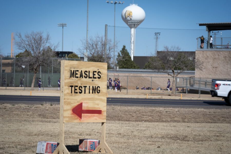 Measles testing sign in Seminole, Texas, during the 2025 measles outbreak, with a school and water tower visible in the background.