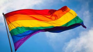 Rainbow Pride flag waving against a blue sky, symbolizing support for Lubbock's LGBTQ+ community and the 2024 Pride Month proclamation campaign led by OUTwest Lubbock