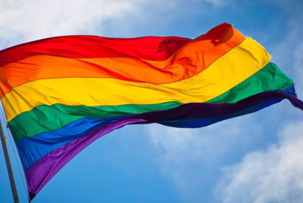 Rainbow Pride flag waving against a blue sky, symbolizing support for Lubbock's LGBTQ+ community and the 2024 Pride Month proclamation campaign led by OUTwest Lubbock