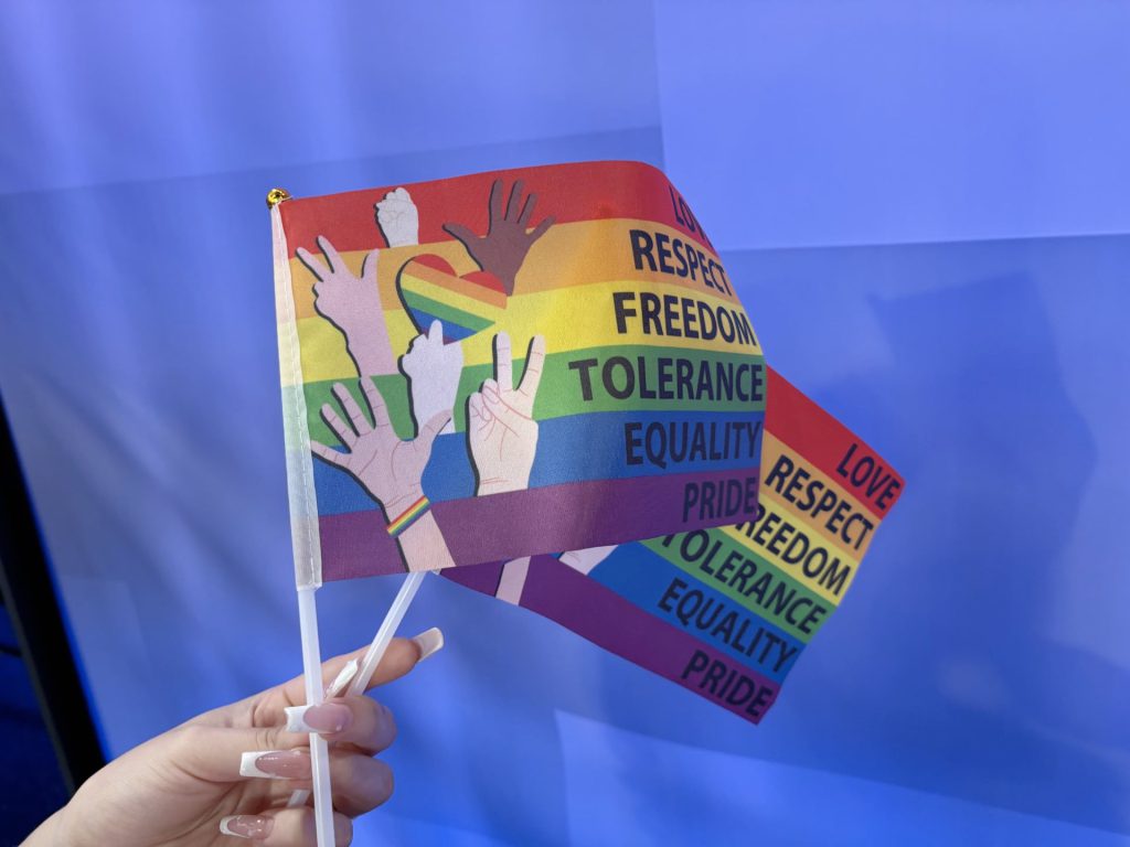 Hand holding a rainbow pride flag with words like love, respect, freedom, tolerance, equality, and pride, during a peaceful sit-in at Lubbock City Council advocating for official Pride Month recognition.