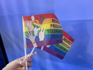 Hand holding a rainbow pride flag with words like love, respect, freedom, tolerance, equality, and pride, during a peaceful sit-in at Lubbock City Council advocating for official Pride Month recognition.
