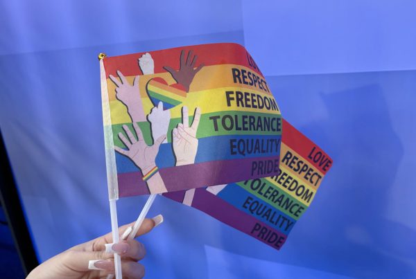 Hand holding a rainbow pride flag with words like love, respect, freedom, tolerance, equality, and pride, during a peaceful sit-in at Lubbock City Council advocating for official Pride Month recognition.