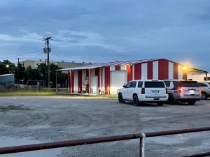 Exterior of a red-and-white metal building in Archer County, Texas, where law enforcement executed a search warrant as part of an illegal gambling and money laundering investigation. Several SUVs are parked outside during the evening.