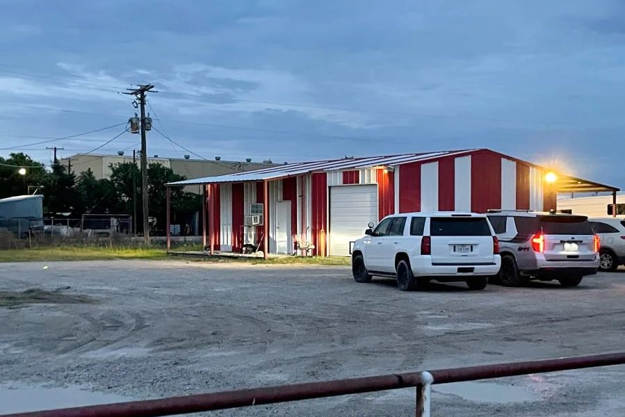 Exterior of a red-and-white metal building in Archer County, Texas, where law enforcement executed a search warrant as part of an illegal gambling and money laundering investigation. Several SUVs are parked outside during the evening.