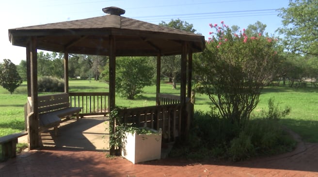 Wooden gazebo at Lubbock Memorial Arboretum surrounded by greenery and blooming shrubs, highlighting need for community volunteers after vandalism incident.