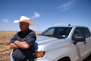 Cotton farmer Walt Hagood stands beside his truck in a dry Texas field, advocating for cotton over synthetic fibers amid rising fast fashion concerns.