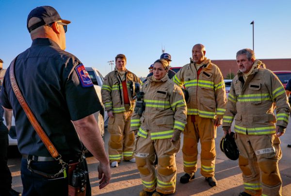 Lubbock firefighters in turnout gear receiving a safety briefing outdoors before training exercise.