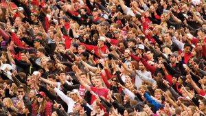 Texas Tech football fans wearing red and black making the Guns Up hand sign during a game day crowd celebration.