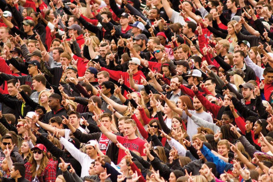 Texas Tech football fans wearing red and black making the Guns Up hand sign during a game day crowd celebration.