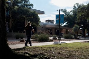 Student walking across Angelo State University campus with trees and ASU banners in view.