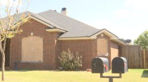 Brick home in Lubbock with windows boarded up after June storm damage.