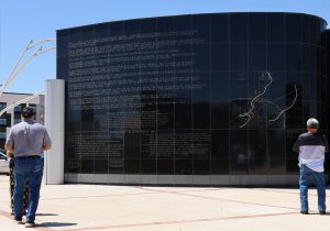 Visitors read the history and storm path map inscribed on the curved black granite wall of the Lubbock tornado memorial, honoring the victims and survivors of the 1970 F5 tornado.
