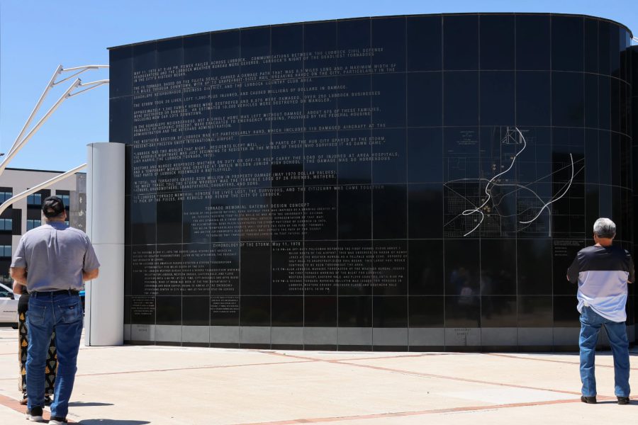 Visitors read the history and storm path map inscribed on the curved black granite wall of the Lubbock tornado memorial, honoring the victims and survivors of the 1970 F5 tornado.