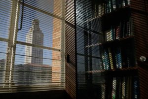 University of Texas at Austin Tower seen through library window blinds with bookshelf inside.