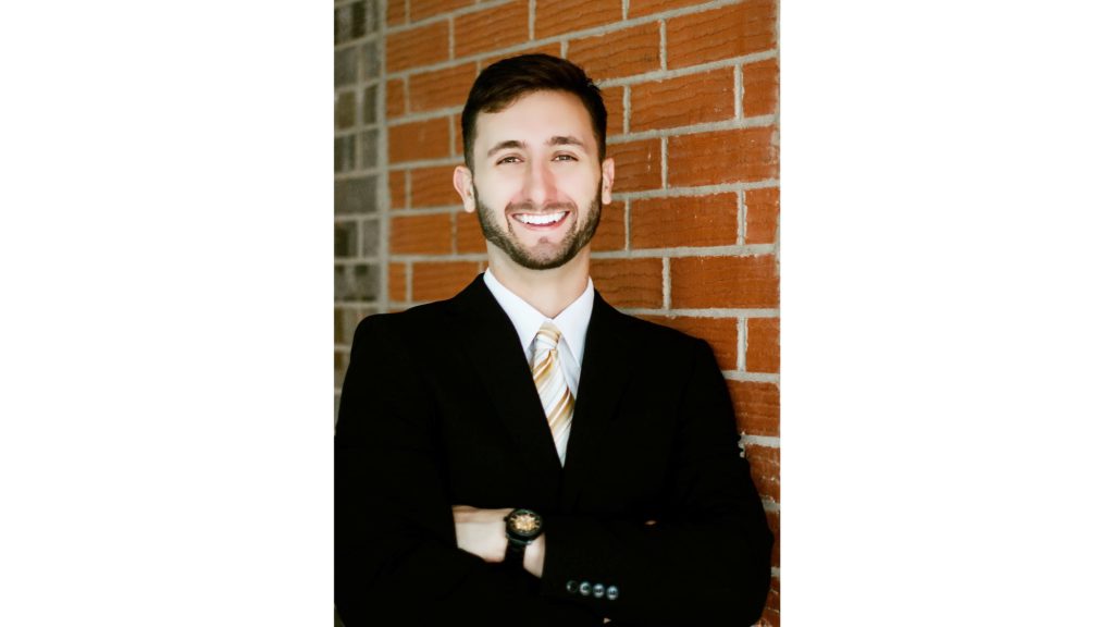 Austin Hughes, owner of Thunder Sun Homes, smiling in a suit while standing against a brick wall in Lubbock, Texas.