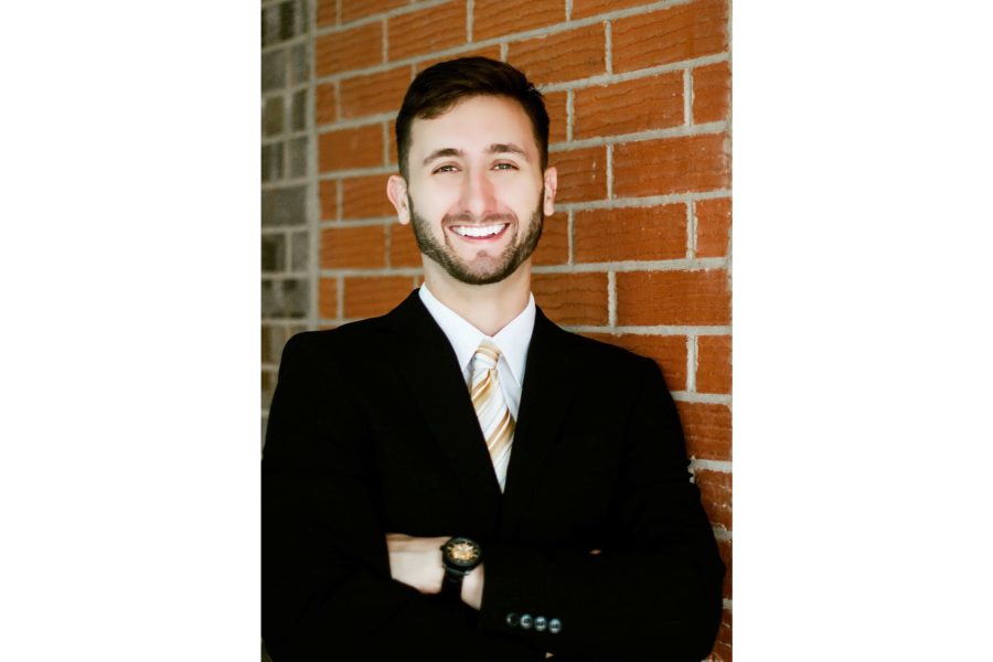 Austin Hughes, owner of Thunder Sun Homes, smiling in a suit while standing against a brick wall in Lubbock, Texas.