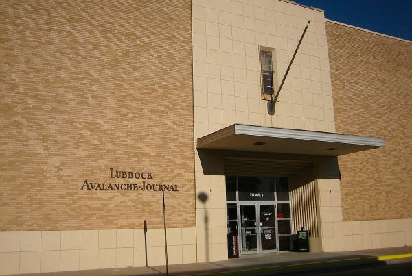 Exterior of the Lubbock Avalanche-Journal building on Avenue J, showing the newspaper’s brick facade and entrance under a clear Texas sky.