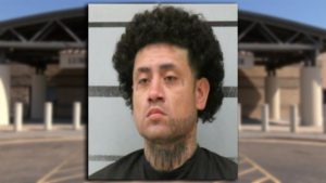 Mugshot of Joe Lopez with curly hair and neck tattoos in front of a jail booking wall.