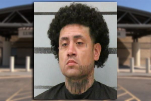 Mugshot of Joe Lopez with curly hair and neck tattoos in front of a jail booking wall.