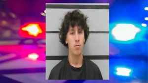 Mugshot of Adrian Castilleja with curly hair in front of a height chart background, with police lights blurred behind him.