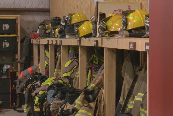 Rows of yellow helmets and turnout gear hanging in a Lubbock County volunteer fire station, highlighting funding cuts to local fire departments.