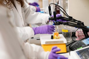 Scientists wearing lab coats and purple gloves testing water samples for PFAS contamination in a laboratory.