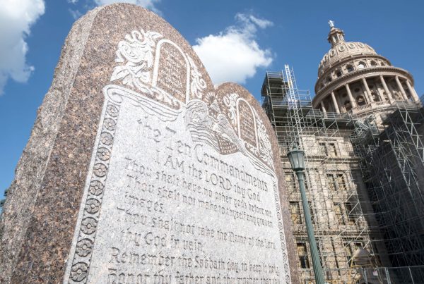 Granite Ten Commandments monument at the Texas State Capitol in Austin, with scaffolding around the dome and a bright blue sky overhead.