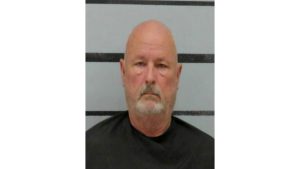 Mugshot of Terry Joe Sides Jr., an older bald man with a gray beard wearing a jail smock, photographed against a height marker background.