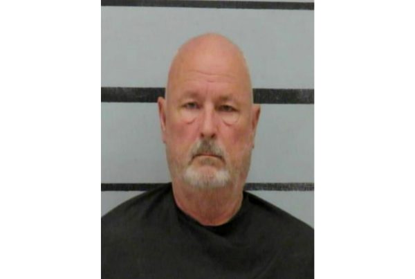 Mugshot of Terry Joe Sides Jr., an older bald man with a gray beard wearing a jail smock, photographed against a height marker background.