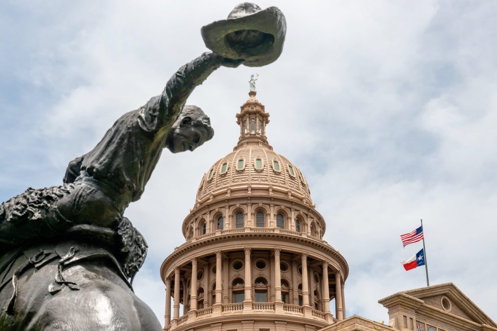 Statue of a cowboy tipping his hat in front of the Texas State Capitol dome in Austin.