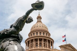 Statue of a cowboy tipping his hat in front of the Texas State Capitol dome in Austin.
