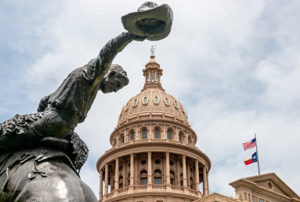 Statue of a cowboy tipping his hat in front of the Texas State Capitol dome in Austin.