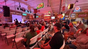 Audience gathered inside Cook’s Garage in South Lubbock for a Turning Point USA rally featuring Texas Attorney General Ken Paxton, surrounded by vintage neon signs and political banners.