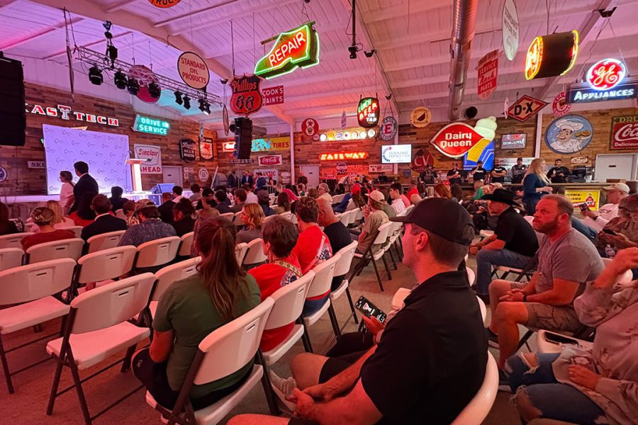 Audience gathered inside Cook’s Garage in South Lubbock for a Turning Point USA rally featuring Texas Attorney General Ken Paxton, surrounded by vintage neon signs and political banners.