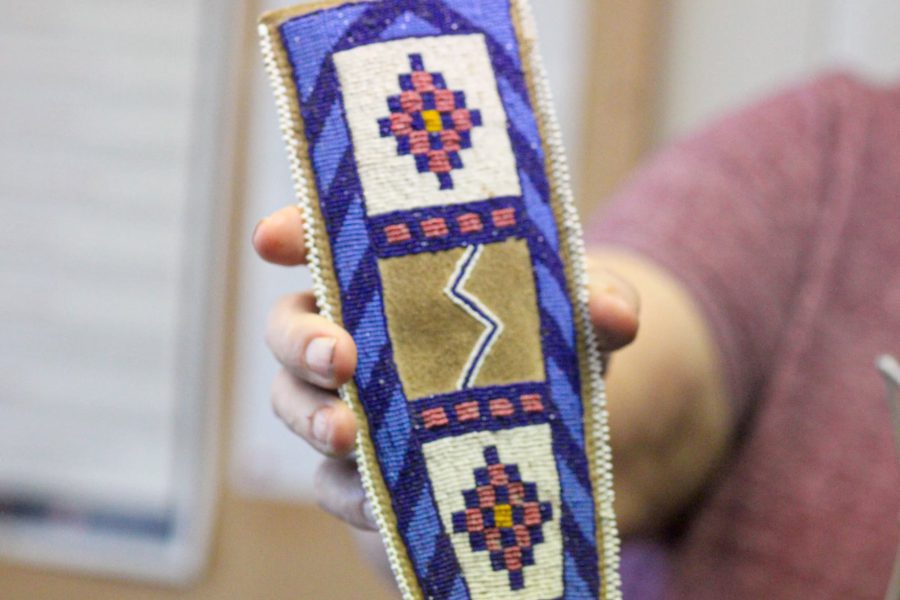 Hand holding a piece of Native American beadwork featuring geometric designs in blue, purple, and tan.