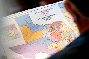 A person reviewing a printed map of proposed Texas U.S. congressional districts, showing color-coded boundaries from plans PLANC2331 and PLANC2333.