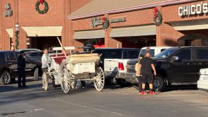 Horse-drawn Christmas carriage involved in a crash with parked vehicles at Kingsgate Center in Lubbock, Texas, as bystanders and police look on.