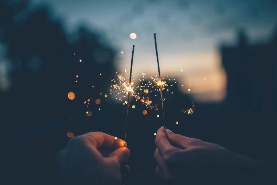Hands holding sparklers at dusk during a New Year’s Eve celebration, with glowing sparks against a darkening sky.