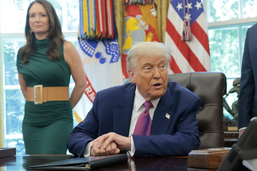 Trump speaking at his desk in the Oval Office while Agriculture Secretary Brooke Rollins stands behind him during an announcement about federal support for farmers in 2025.