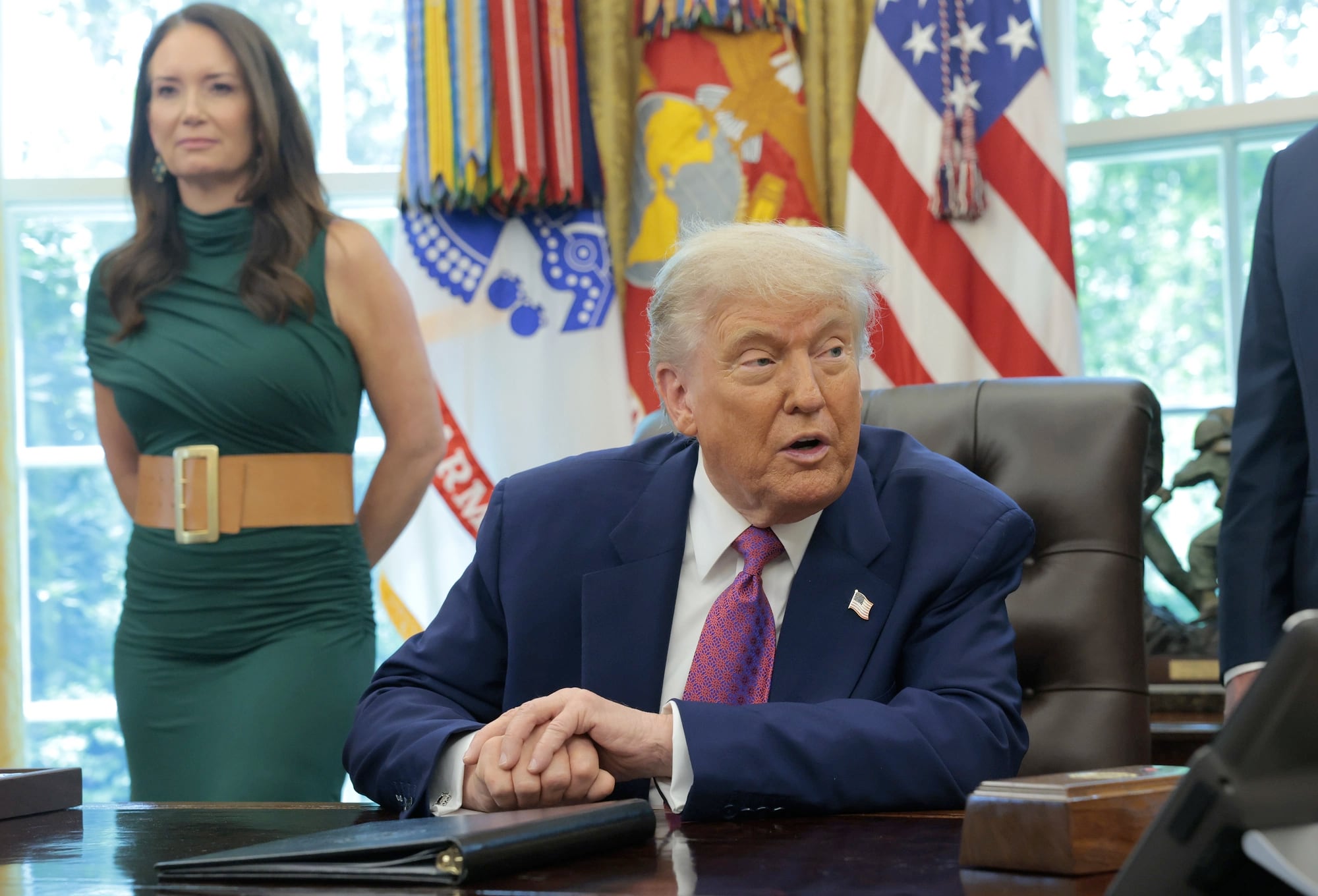 Trump speaking at his desk in the Oval Office while Agriculture Secretary Brooke Rollins stands behind him during an announcement about federal support for farmers in 2025.
