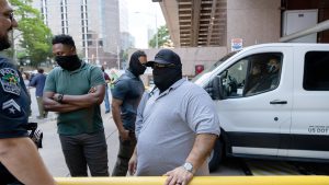 Masked ICE agents and local police stand near a white enforcement vehicle during a public immigration operation in a Texas city.