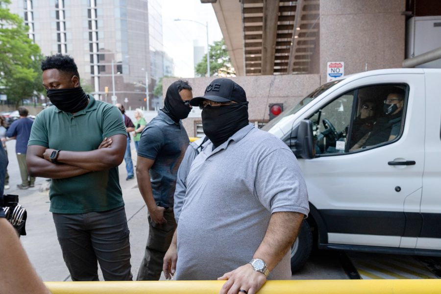 Masked ICE agents and local police stand near a white enforcement vehicle during a public immigration operation in a Texas city.