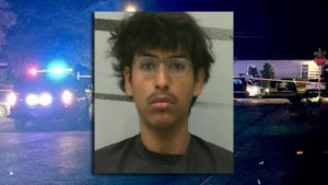 Booking photo of Adam Villarreal charged in a Central Lubbock drive-by shooting case, with police lights in the background.