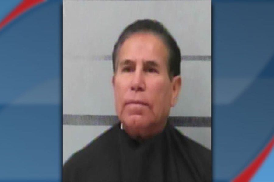 A booking photo of 70-year-old Raymundo Almaraz, wearing a black garment against a grey background with horizontal lines.