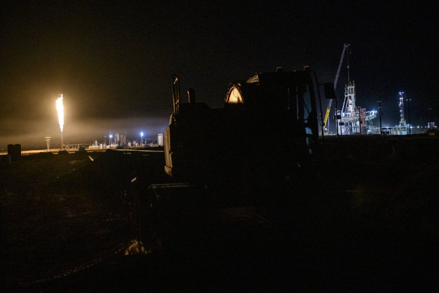 Nighttime oil and gas drilling site in West Texas with active flaring illuminating rigs and industrial equipment under a dark sky.