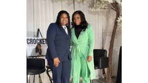 Texas Representative Jasmine Crockett in a green outfit stands smiling next to 15-year-old Brooklyn, who is wearing a navy suit, during a campaign stop in Lubbock.